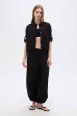 Camisa negra de viscosa, holgada, con mangas cortas abotonadas, cuello camisero, detalles de cintas decorativas verticales y cierre frontal con botones.