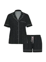 Pijama corto negro con estampado de lunares blancos, compuesto por una camisa de manga corta abotonada con ribetes blancos y un short a juego con cordón de ajuste rosado.