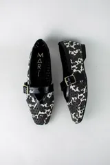 Guillerminas flat de ecocuero caladas, con diseño estampado animal print blanco y negro, tira en el empeine con hebilla dorada y ribetes de charol negro.