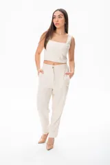 Pantalón de vestir color crudo, de corte recto, con bolsillos laterales y traseros. Se ajusta a la cintura con cinturón de cuero marrón.