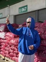Canguro de tela deportiva color azul con capucha y cordones ajustables en color rosa. Presenta el logo bordado en color rosa en el pecho.