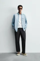 Camisa de corte regular fit confeccionada en denim ligero de algodón con efecto lavado. Presenta cuello solapa con botones, manga larga con puños abotonados, cierre frontal de botones y un bolsillo plastrón en el pecho.