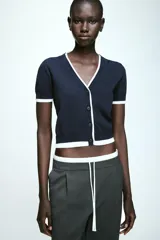Chaqueta de punto de manga corta con escote en pico y cierre frontal con botones. Presenta un diseño en color azul marino con bordes en contraste de color blanco en el cuello, la tapeta de botones, los puños y el ruedo.