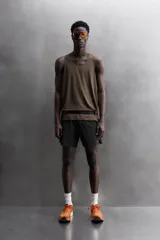 Pantalón corto deportivo color marrón oliva, confeccionado en tejido técnico ligero y elástico, con forro interior. Presenta cintura elástica ajustable con cordón, bolsillos frontales, bolsillo de seguridad trasero con cierre y aberturas laterales en el bajo.