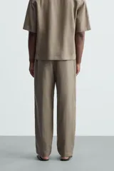 Pantalón de calce relajado confeccionado en tejido de viscosa y yute color tostado. Presenta cintura elástica ajustable con cordón, bolsillos laterales, bolsillos traseros de vivo y cierre frontal con cremallera y botón.