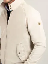 Campera Harrington color beige, con cuello alto abotonado, cierre frontal completo y bolsillos laterales con solapa y botones a presión. Puños y cintura elastizados de rib.