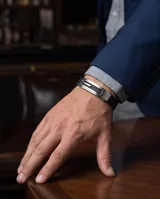 Pulsera masculina con diseño moderno, compuesta por una banda central de acero inoxidable con detalles calados y laterales de cuerina negra texturizada.