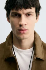 Cazadora de hombre de corte regular fit, color marrón oscuro, confeccionada en tejido efecto ante. Presenta cuello solapa, manga larga con puño abotonado, dos bolsillos de plastrón con solapa en el pecho y bolsillos laterales en la costura de la cadera. Cierre frontal con botones a presión.