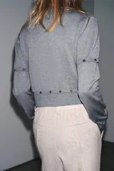 Jersey de punto de cuello redondo y manga larga, con diseño cropped. Presenta detalles de costuras con botones que permiten desmontar partes de la prenda en las mangas y en la cintura.
