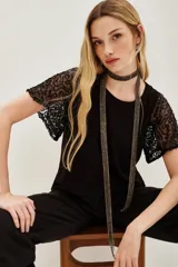 Remera negra de algodón con mangas cortas de encaje bordado con lentejuelas negras. Presenta un diseño de cuello redondo y corte clásico.