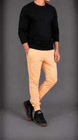 Pantalón tipo jogger color naranja claro, con ajuste elástico en los tobillos, bolsillos laterales y logo bordado pequeño en la parte superior.