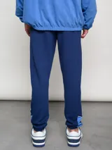 Pantalón deportivo azul claro con puños ajustados en los tobillos. Presenta el escudo del Club Nacional de Football bordado en la pierna izquierda y el logo de Umbro bordado en la derecha.