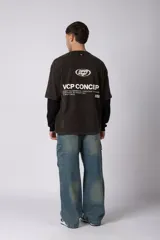 Remera de doble capa con diseño de efecto superpuesto. La capa exterior es de algodón con lavado acid wash en color gris oscuro y cuenta con un logo ovalado estampado en el pecho. La capa interior es de manga larga en color negro liso. Presenta un corte relajado y cuello redondo.