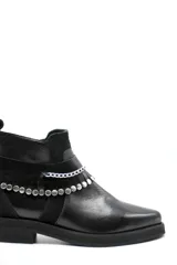 Bota corta tipo chelsea de cuero negro, con paneles laterales de gamuza y suela plana de goma. Presenta un diseño minimalista con tirador en la parte trasera.