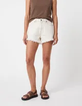 Short de denim color off white, de tiro medio con bolsillos delanteros y traseros, cierre frontal con botón y cremallera, y terminación de flecos en el ruedo.