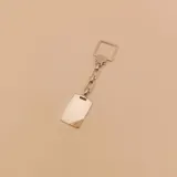 Llavero plateado con dije rectangular con detalle dorado en una esquina, unido por una cadena de eslabones a un aro cuadrado.