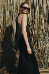 Vestido largo de satén negro con cuello halter subido y espalda descubierta. Presenta un diseño fluido con bajo en línea evasé.