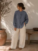 Camisa negra de calce relajado con cuello mao, cierre frontal de botones y detalle de volado vertical en el frente. Presenta mangas largas con puños abotonados.
