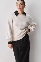 Sweater negro de tejido suave con escote redondo, mangas largas y calce relajado, con terminaciones acanaladas en cuello, puños y ruedo.