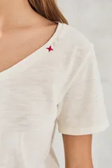 Remera básica de algodón peinado color marfil, de manga corta y cuello en V, con detalle de pequeño bordado rojo en el escote.
