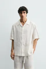 Camisa negra de manga corta, confeccionada en lino con corte relaxed fit, cuello bowling y cierre frontal de botonadura.