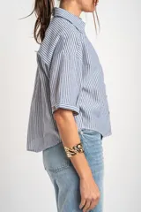 Camisa de manga corta con patrón de rayas verticales en tonos azul y blanco, cuello camisero y cierre frontal con botones.