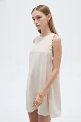 Vestido corto sin mangas en tono beige natural, con cuello redondo y volados delicados en las sisas.