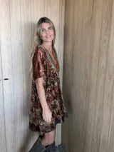 Vestido midi de terciopelo con estampado en tonos tierra y verdes. Presenta un corte holgado, mangas cortas y un escote en V destacado por un aplique artesanal de cuero en tonos verdes y marrones, unido con bordados a mano.
