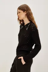 Sweater negro de punto calado con cuello polo decorado con apliques de piedras brillantes de colores. Presenta mangas largas con puños ajustados y un diseño elegante.