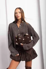 Cartera tipo baguette de gamuza color chocolate, con diseño decorado con diversos apliques metálicos, perlas y piezas de piedra. Cuenta con cierre superior y correa ajustable.