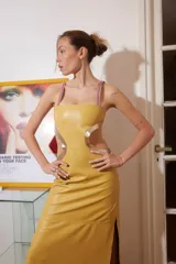 Vestido midi de cuero color maíz con cortes laterales y detalles dorados. Tiene tiras finas fucsias y abertura lateral en la falda.