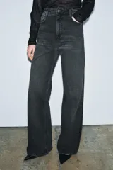 Jeans de tiro alto con corte wide leg y largo completo. Presenta diseño de cinco bolsillos, trabillas en la cintura y cierre frontal con cremallera y botón, con un acabado de efecto lavado.