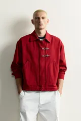 Cazadora relaxed fit de Zara confeccionada en tejido de algodón rojo con efecto lavado. Presenta cuello solapa, manga larga, bolsillos de plastrón en la cadera y cierre frontal de cremallera oculta con solapa y alamares metálicos.