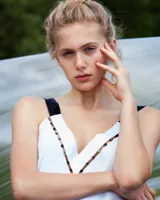 Vestido corto blanco de gasa y seda fina, con escote pronunciado y apliques de perlas de vidrio. Espalda abierta con tirantes cruzados anchos y caída asimétrica.