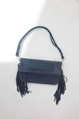Cartera bandolera de gamuza azul marino con flecos en los laterales y solapa frontal decorada con detalle de cuero liso. Cuenta con asa ajustable y herrajes metálicos plateados.