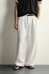 Pantalón relaxed fit de color blanco off-white, confeccionado en tejido con lino. Cuenta con pliegues frontales en la cintura, bolsillos delanteros y cierre frontal con cremallera y botón.