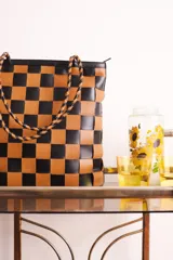 Bolso tipo tote de cuero trenzado a mano con diseño de damero en colores marrón y beige. Cuenta con doble asa trenzada y forro interior.