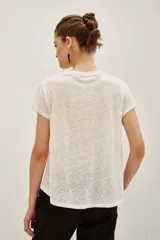 Remera de lino color blanco con detalle de encaje en el escote y hombros, de corte holgado y mangas cortas.