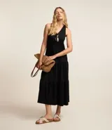 Vestido midi de corte evasé confeccionado en tejido piquet color negro. Presenta un diseño sin mangas con escote en V, breteles anchos cruzados en la espalda con detalle de nudo y falda con recortes de volados en la parte inferior.