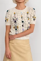 Sweater de manga corta de lana merino color marfil, con cuello redondo, diseño texturizado en relieve y bordados florales multicolores hechos a mano.