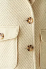 Abrigo de cuello sastre color beige, con forro, cierre frontal con botones, bolsillos con solapa y presillas en mangas. Confeccionado en lana fina sin teñir, diseñado exclusivamente por Don Baez.