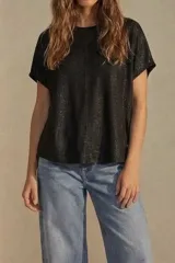 Remera negra de corte oversize, con cuello redondo y mangas cortas. Presenta una textura sutilmente brillante y una costura vertical central en el frente.