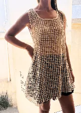 Vestido corto sin mangas, color beige claro, confeccionado en tejido calado con patrón de pequeñas flores repetidas. Presenta escote redondo y corte holgado.