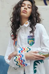 Camisa blanca de corte oversize con bordados de motivos playeros y mangas largas con puños decorados con ondas de colores.