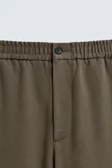 Pantalón regular fit color marrón oscuro, confeccionado en tejido con viscosa. Cuenta con cintura elástica, bolsillos delanteros y detalle de bolsillos traseros de vivo. El cierre frontal es con cremallera y botón.