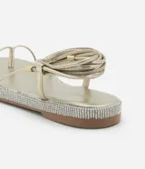 Sandalias planas doradas con tiras finas, lazo para atar al tobillo y suela forrada en cristales.
