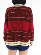 Cardigan tejido de punto jacquard en tonos bordó y rojo con rayas, de corte oversize, cuello redondo y cierre frontal con botones carey. Presenta detalles bordados en contraste y monograma en la espalda.