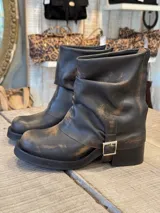 Bota corta de cuero con efecto desgastado, color marrón oscuro con matices bronceados. Presenta un diseño de caña arrugada y una tira lateral ajustable con hebilla metálica plateada. Cuenta con suela de goma gruesa y taco cuadrado.