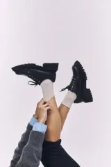 Zapatos de cuero negro con cordones, diseño robusto y suela track dentada. Presentan un detalle metálico en el centro de los cordones.