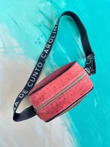 Bandolera Kaira de la línea Ottenta de Carolina De Cunto, confeccionada en cuero color rojo con diseño estilo splash en negro y bolsillo frontal superior en tono cobre. Cuenta con correa larga regulable negra con el nombre de la marca en blanco y cierre superior con cremallera.